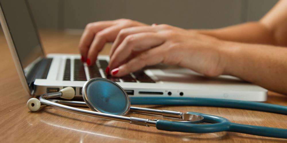 stethoscope with woman's hands typing on computer